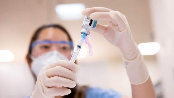 Nurse wears gloves and moves covid vaccine into syringe.